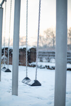 A Lonely Snow-covered Metal Chain Swing On A Playground In The Winter Morning Sunlight. 