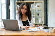 © Wasana - Black businesswoman sitting in front of laptop in office, Check operating results documents and accounting documents