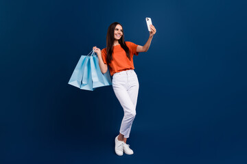 Poster - Full length photo of sweet shiny lady wear orange t-shirt holding bargains recording video vlog device isolated dark blue color background