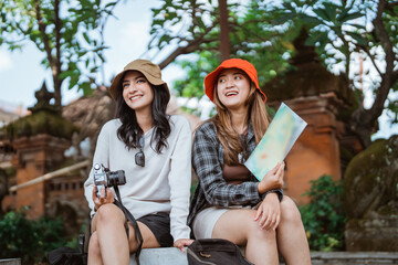 two attractive local tourists sit holding a map and a camera in front of a religious temple