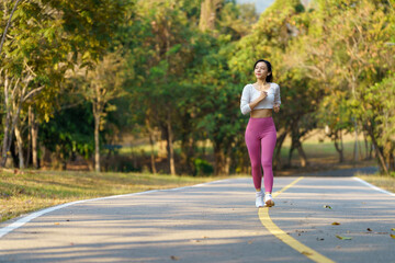  Asian woman jogging in the park smiling happy running and enjoying a healthy outdoor lifestyle. Female jogger. Fitness runner girl in a public park. healthy lifestyle and wellness being a concept.