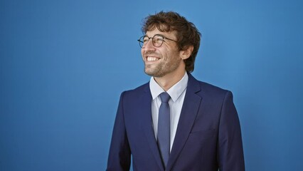 Canvas Print - Young man wearing business suit looking away to side with smile on face, natural expression. laughing confident. over isolated blue background