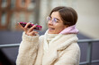 Beautiful young woman, student in braces stands outdoor and talking on phone against blurred background with cityscapes. Concept of beauty care and medicine, gadgets, blogging, leisure time.