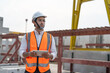 © Supachai - Confident male civil engineer wearing safety vest with white helmet standing and holding tablet working at factory or construction site making precast concrete wall for real estate housing