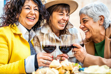 Wall Mural - Happy senior women drinking red wine at bar restaurant - Mature people having fun hanging out on city street - Life style concept with older friends smiling and laughing together	
