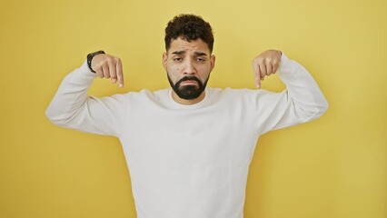 Wall Mural - Pathetic young man, isolated, looking sad and miserable as he's pointing down with his fingers on yellow background, reflecting his dwelling in the direction of unhappiness