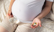 A pregnant girl holds pills in her palm and another glass of water. Concept of taking vitamins, iron and folic acid during pregnancy, close-up