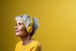 Portrait of a happy senior woman listening to music with headphones on yellow background. Hipster. Music Streaming Service Concept with Copy Space.