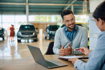 Young man discussing about terms of agreement with car saleswoman in showroom.