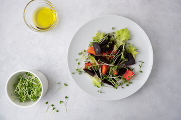 A healthy salad made from boiled beets, carrots, micro greens and lettuce. Dish on a light gray background and a white plate with olive oil and microgreens. Fresh tasty dish for healthy eating