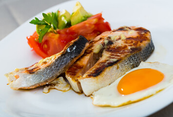 Wall Mural - Grilled salmon served with fried egg, fresh tomatoes, avocado and parsley on white dish..