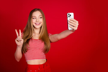 Wall Mural - Photo of pretty cute girl wear striped top showing v-sing tacking selfie empty space isolated red color background