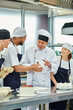 © LIGHTFIELD STUDIOS - mature good looking chief cook in white hat helping his interracial chefs with dough, confectionary