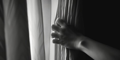 Poster - A black and white photo of a person's hand resting on a curtain. Suitable for various themes and concepts