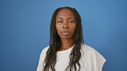 Wall Mural - Serious african woman with curly hair wearing a white shirt against a blue wall in a portrait