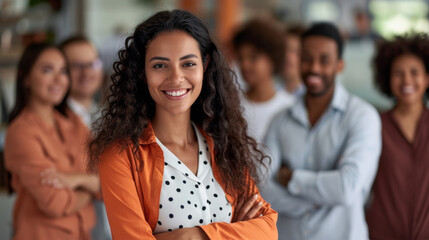 Canvas Print - Professional team, with a woman in the foreground smiling confidently at the camera, arms crossed, and her team in the background.