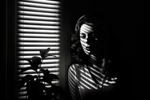 Black And White Portrait Photograph Of A Woman Next To A Window With Closed Blinds, Contrasting Lights And Darks. From The Series “Art Film - Black And White," "The Lovely Ladies," "Trouble."