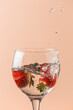 strawberry falling into the balloon cup, the background is salmon-colored and there are water drops