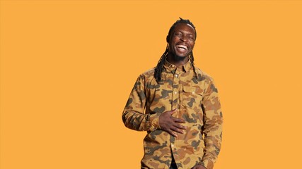 Wall Mural - Cheerful adult enjoying shoot and laughing on camera, making jokes in studio and acting playful. Silly positive african american guy having fun over orange background, relaxed casual person.