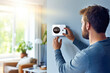 Young adult male fine-tuning a smart home thermostat in a contemporary, bright sun lit living space. Concept of smart home technology for everyday comfort living and domestic life. Copy space