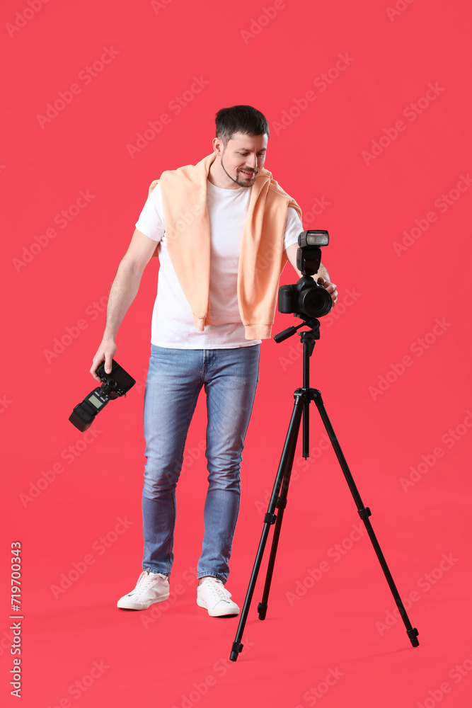 Male photographer with professional cameras on red background