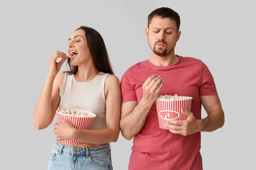 Canvas Print - Happy young couple eating popcorn on light background