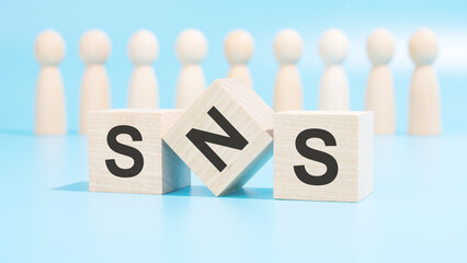 Poster - forming a conceptual word with cubes in the foreground - SNS. the cubes are located on a blue surface in front of wooden figures symbolizing people.