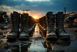 As the sun sets on the outdoor horizon, a row of black boots stand tall against the sky, their reflection shimmering in the water below, representing strength and resilience in the face of changing t