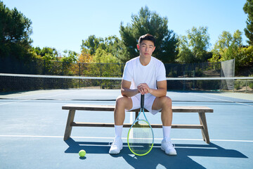 An asian man plays tennis on a court surrounded by trees