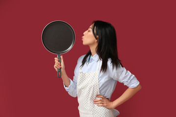 Poster - Portrait of young Asian woman with frying pan on red background