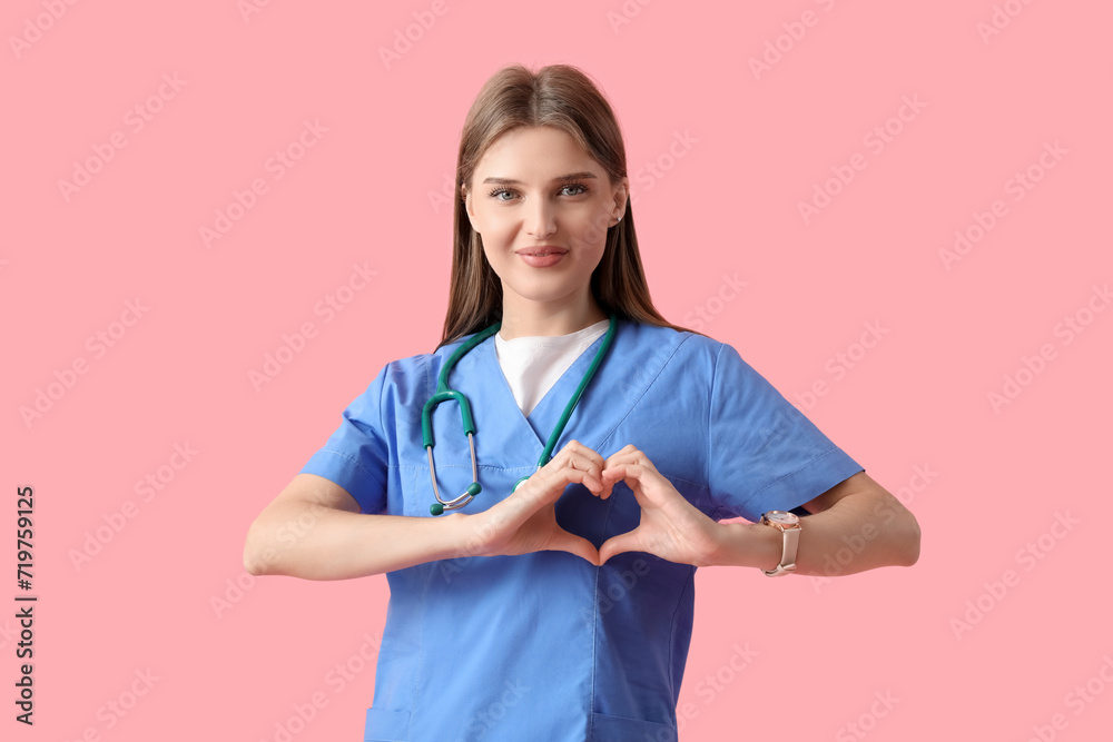 Beautiful doctor making heart gesture on pink background