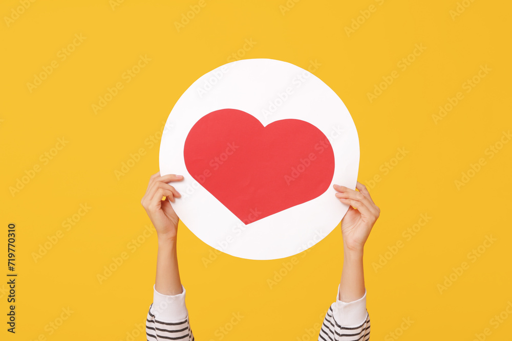 Female hands with heart like icon on yellow background