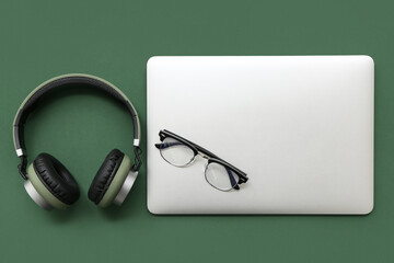 Wall Mural - modern laptop, headphones and eyeglasses on green background