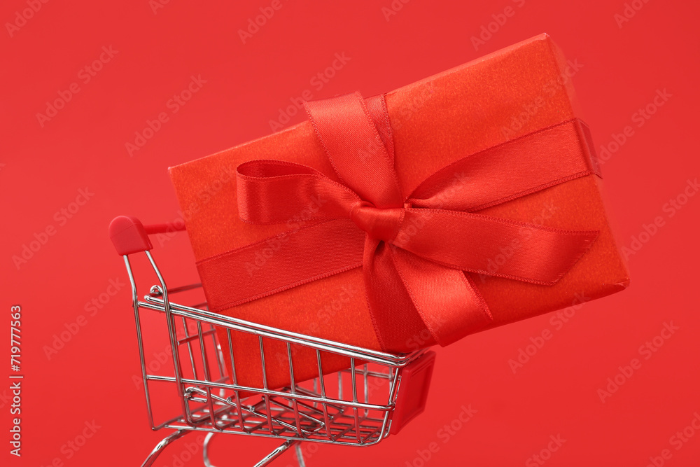 Small shopping cart with gift box on red background. Valentine's Day celebration
