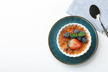 Wall Mural - Delicious creme brulee with berries and mint in bowl on white wooden table, top view. Space for text