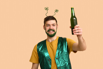 Wall Mural - Young man in headband with green beard holding bottle of beer on beige background. St. Patrick's Day celebration