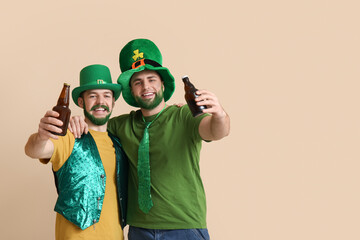 Wall Mural - Happy young men in leprechaun hats with green beards holding bottles of beer on beige background. St. Patrick's Day celebration