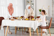 © Pixel-Shot - Young Muslim woman with her mother and little daughter setting table at home. Ramadan celebration