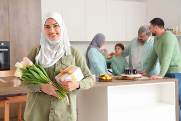 Canvas Print - Young Muslim woman with gift and tulips in kitchen. Ramadan celebration