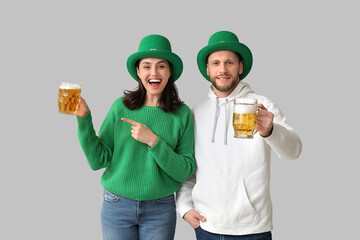 Wall Mural - Beautiful young couple in leprechaun hats pointing at glasses of beer on grey background. St. Patrick's Day celebration