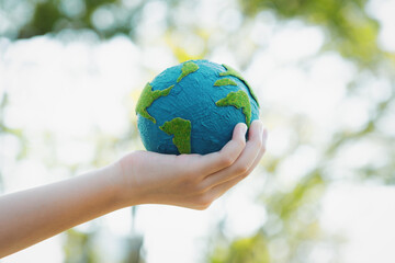 Young boy's hand holding planet Earth globe at natural park background as Earth day to save this planet with ESG principle and environment friendly energy for brighter future. Gyre