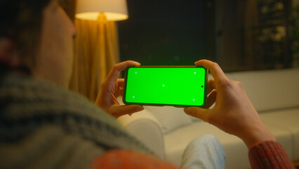 young man watching video on his smartphone with green screen mock up display, which he holds horizon