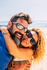 Wall Mural - happy and healthy couple of people enjoying their life and their vacations outdoors at the beach together taking a selfie with the sea or ocean in  background - two happy people taking a picture 