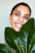 Green beauty skin care portrait. Cleansing. Organic skincare. Indian beautiful young model is posing with a huge green tropical leaf