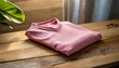 © Asad - a tasteful and inviting scene featuring a blank pinkt-shirt casually laid on a wooden surface. Focus on capturing the textural details of both the fabric and the wood, infusing the composition with