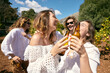 © Just images - Cheers to Sunshine and Laughter. A spontaneous toast under the open sky, as friends in white laugh and clink beer bottles together in an orchard, embodying the spirit of a carefree summer day.