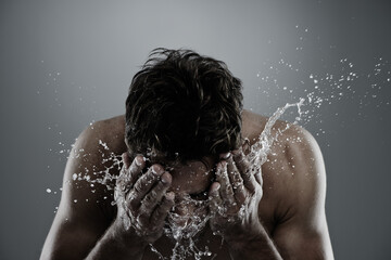 Poster - Water, splash and man cleaning face for bathroom routine, cleanse or fresh skincare in morning beauty treatment. Studio, skin hydration and model facial wash, hygiene and grooming on grey background