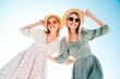 Two young beautiful smiling hipster woman in trendy summer dress. Carefree women in the street in hats. Positive models at sunset. Cheerful and happy. Bottom view. They look at camera from above