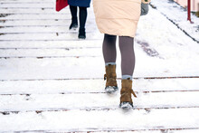 Female Climbing Up Snowy Steps. Snow Covered Stair. Woman Climbs Snow Covered Staircase. Rear View On Woman Legs In Wool Tights And Suede Boots Climbing Slippery Snowy Stairs. Dangerous Winter Walking