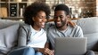 Multiracial young couple bonding, enjoying cozy time watching laptop on sofa at home